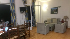 A living room with a wooden dining table, two grey armchairs, a sofa, and a TV mounted on the wall. - Comfortable apartments with swimming pool facing the sea. Ref. Cala Llevadó-46 (Tossa del mar)