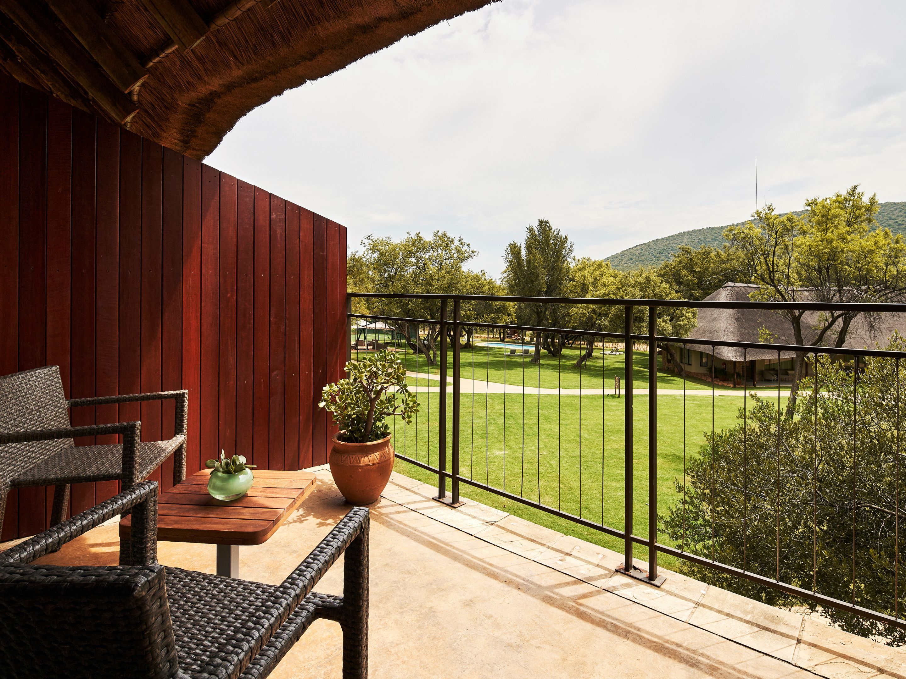 A balcony with a view of a green lawn and a building with a thatched roof.