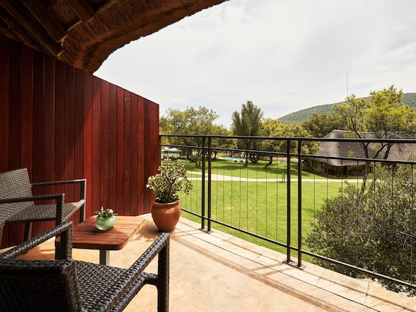 Ein Balkon mit Blick auf eine grüne Wiese und ein Gebäude mit einem Strohdach.