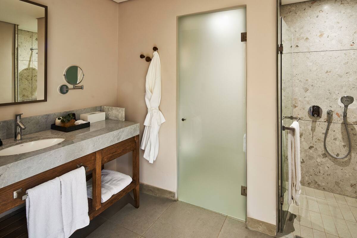 Une salle de bain dotée d’un meuble-lavabo en marbre, d’un meuble-lavabo en bois, d’une cabine de douche en verre et d’une porte en verre dépoli.