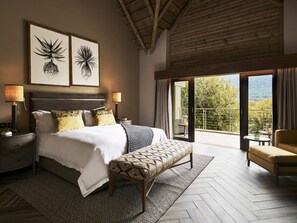 A bedroom with a large bed, two bedside lamps, a bench, and a balcony with a view. - Letamo at Qwabi Private Game Reserve by Newmark (Thabazimbi)