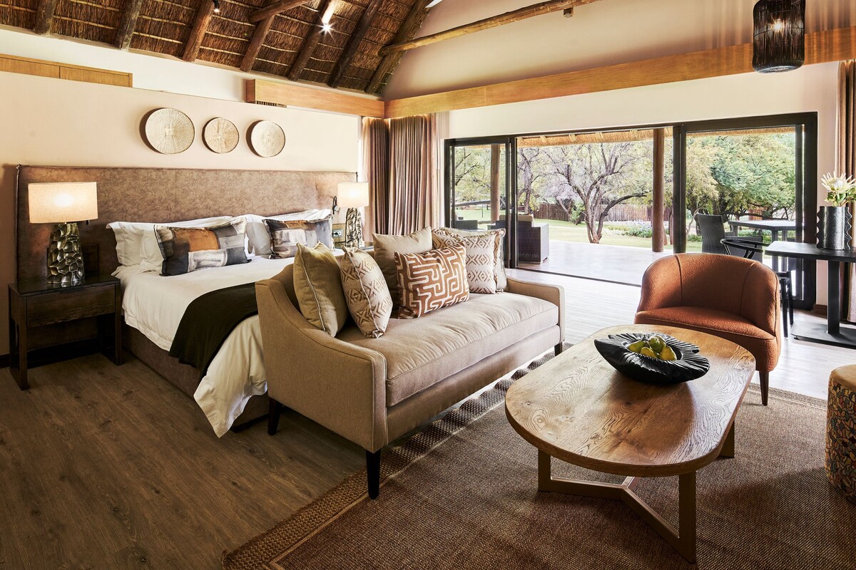 A hotel room with a bed, a sofa, a dining table, and a view of the outdoors.