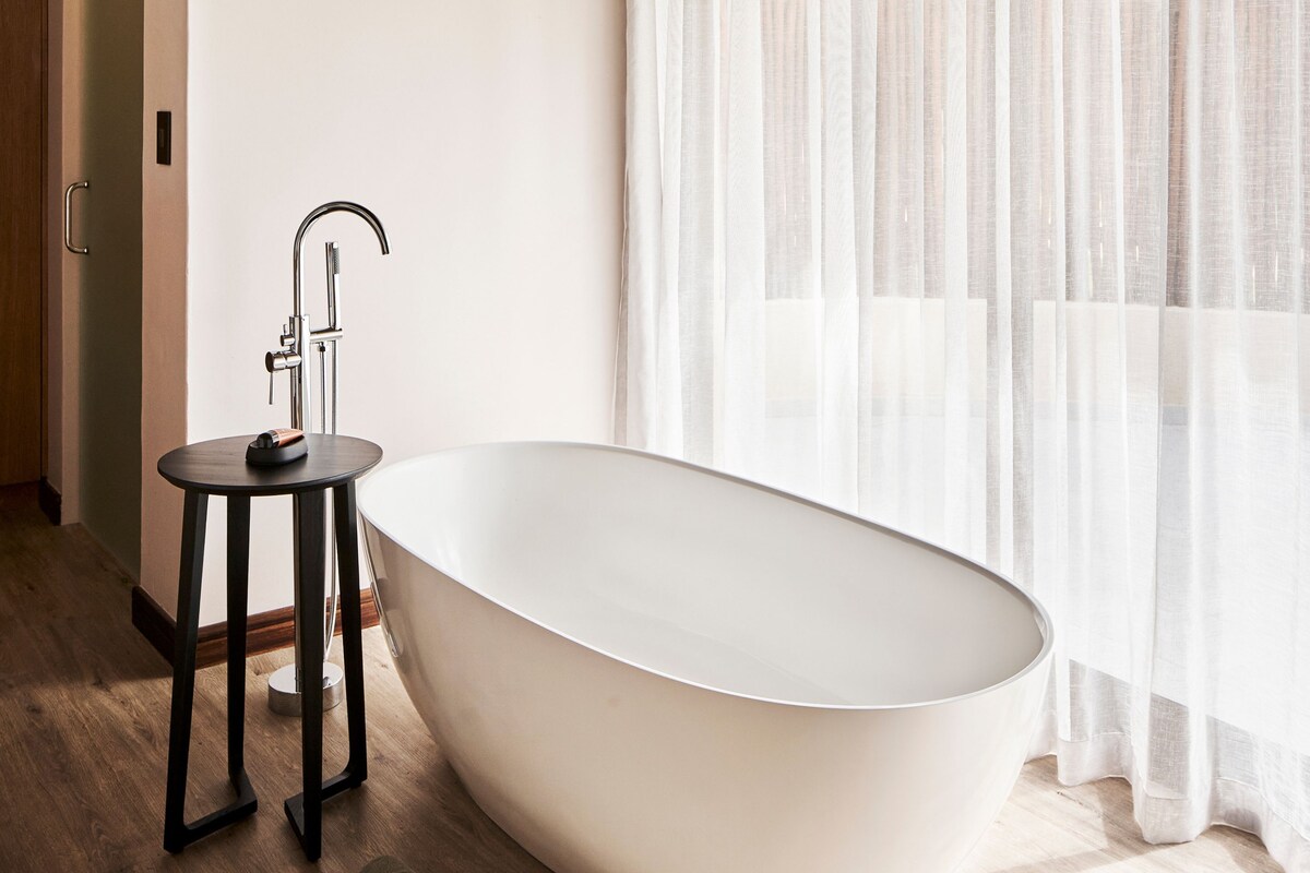 A modern bathroom with a freestanding bathtub, a small round table, and a faucet.