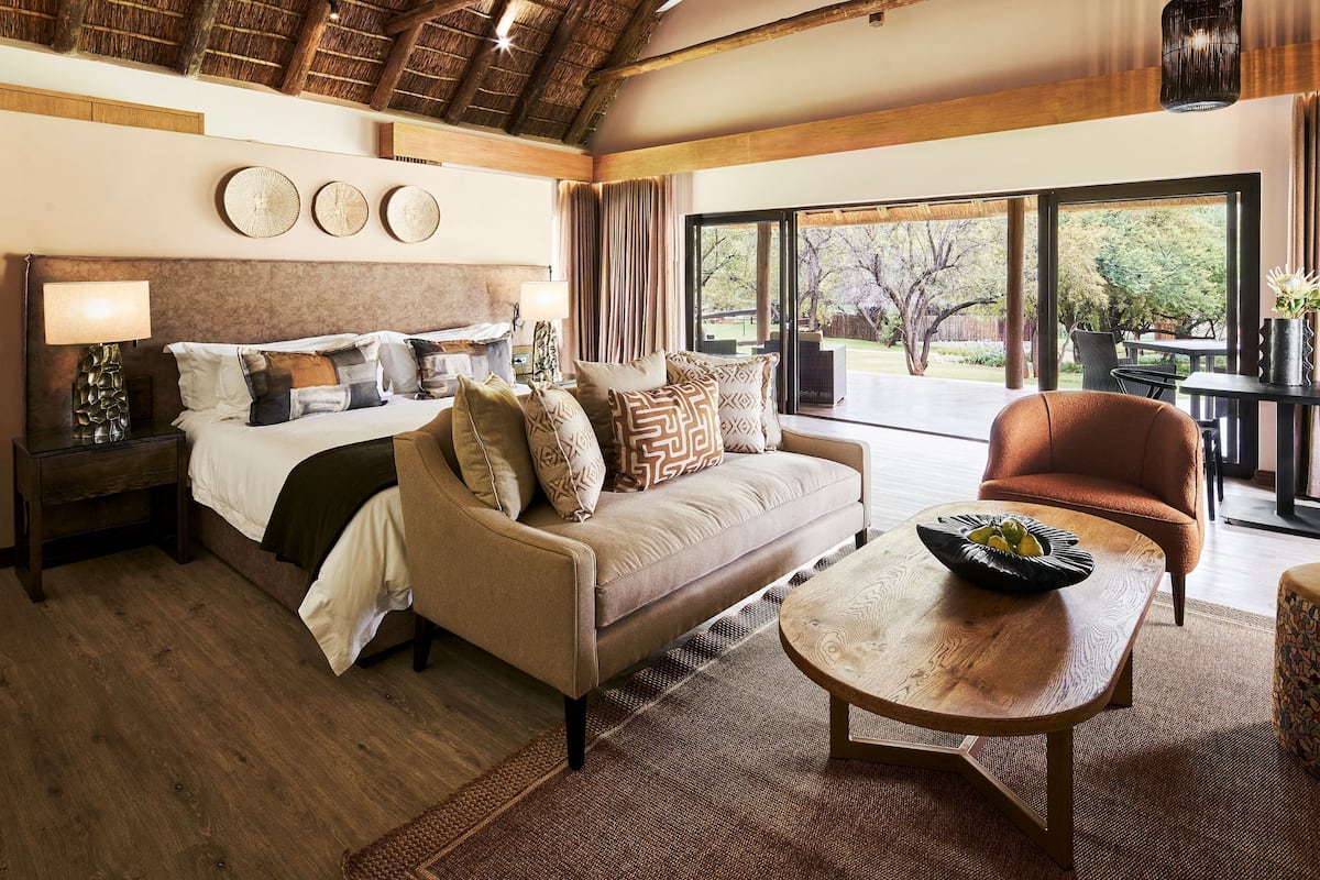 A well-lit room with a bed, a sofa, a coffee table, and a dining area with a view of the outdoors.