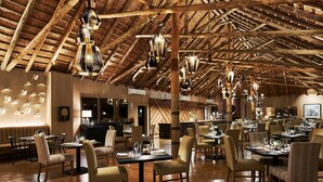 A spacious restaurant with high wooden ceilings and hanging pendant lights. Tables are set with chairs, and the floor is wooden. - Letamo at Qwabi Private Game Reserve by Newmark (Thabazimbi)