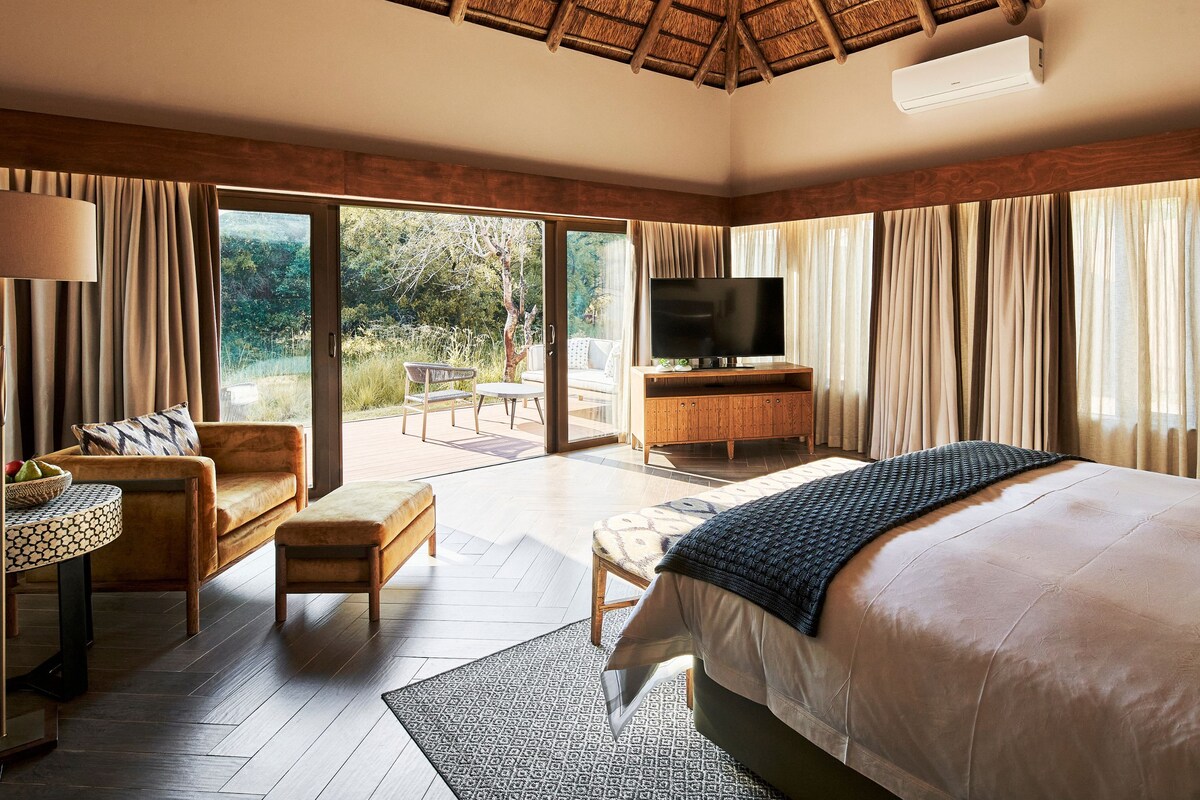 A bedroom with a large bed, a TV, a wooden cabinet, and a seating area with a table and chairs.