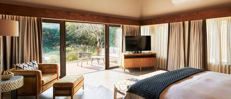 Un dormitorio con una cama grande, televisión, mueble de madera y una zona de estar con mesa y sillas.
