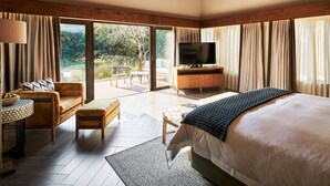 A spacious bedroom with a large bed, a TV, and a seating area with a view of the outdoors. - Letamo at Qwabi Private Game Reserve by Newmark (Thabazimbi)