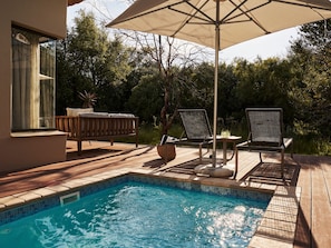 Una piscina con terrazza in legno, lettini e un tavolo.