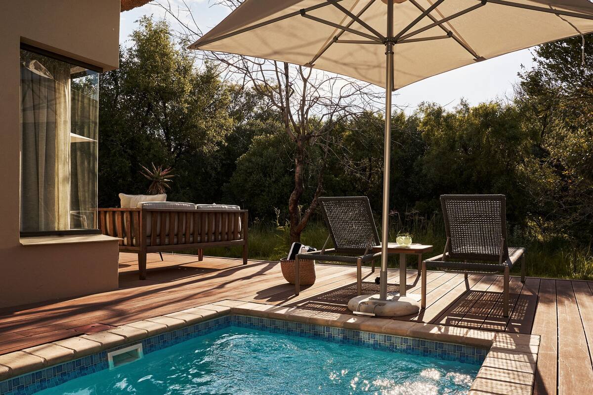 Un espace aménagé au bord de la piscine, avec une terrasse en bois, une chaise longue, une table et un parasol.