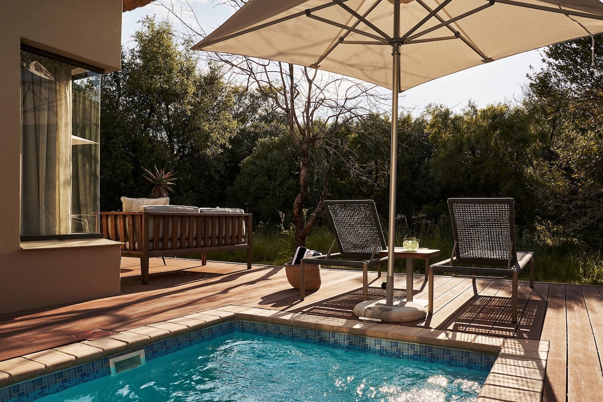 A poolside area with a wooden deck, a lounge chair, a table, and an umbrella.