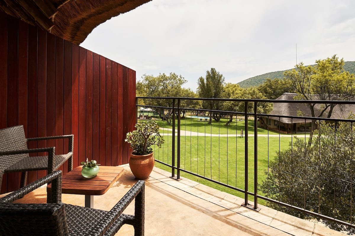 A balcony with wicker furniture, a potted plant, and a view of a golf course and buildings.