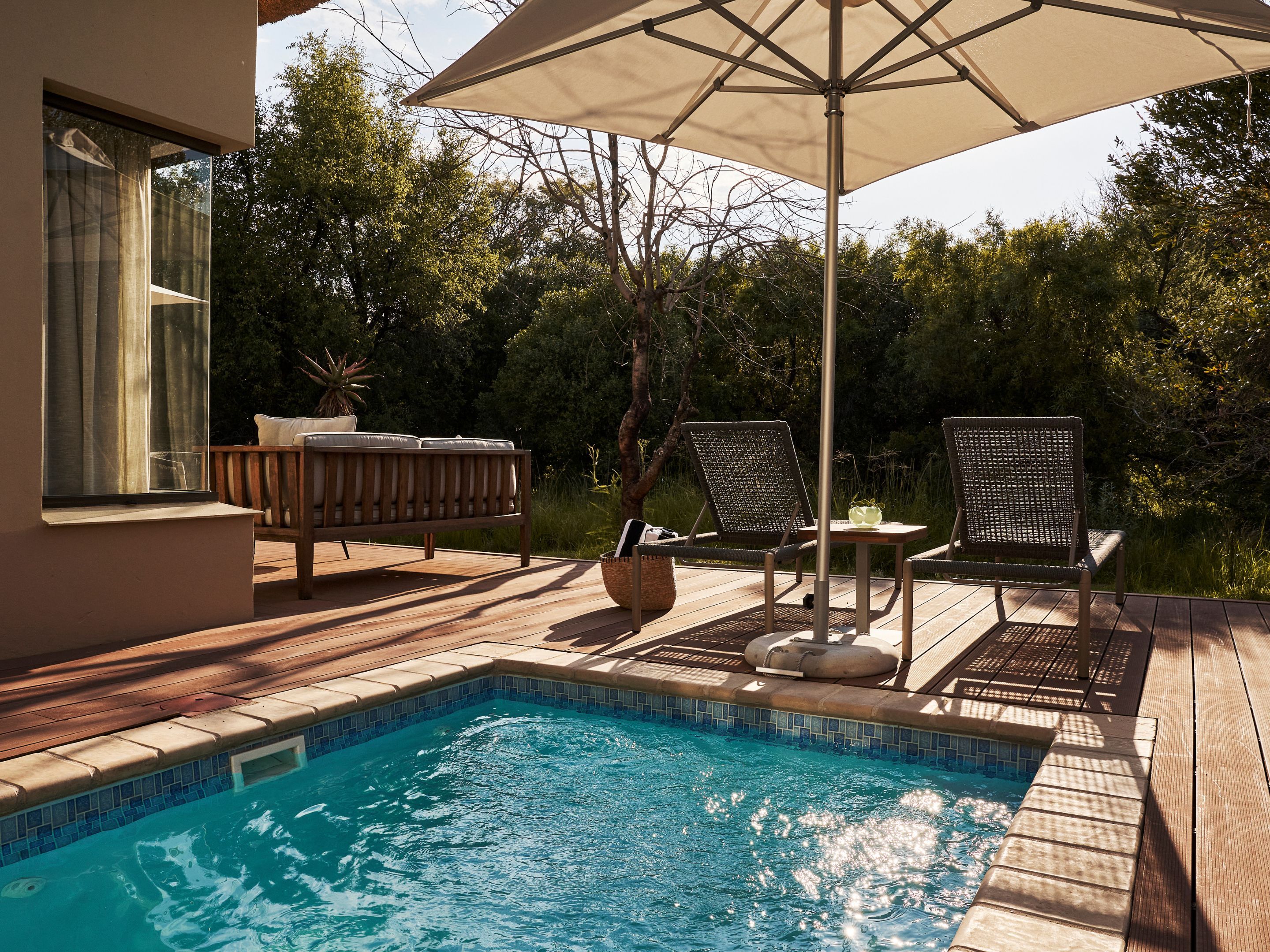 A poolside area with a wooden deck, a lounge chair, a table, and an umbrella.