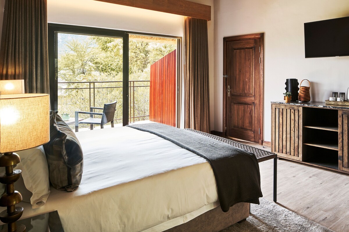 Ein Schlafzimmer mit einem Bett, einem Nachttisch, einer Lampe, einer Tür und Blick ins Freie.