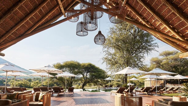 A poolside area with lounge chairs and umbrellas, a thatched roof, and hanging light fixtures. - Letamo at Qwabi Private Game Reserve by Newmark (Thabazimbi)