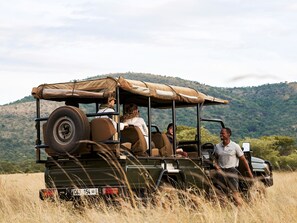 A safari vehicle with passengers, a license plate, and a hilly landscape in the background.