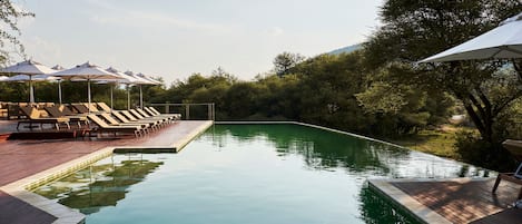 A swimming pool with lounge chairs and umbrellas, surrounded by trees.