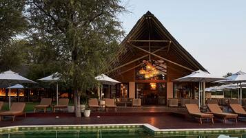 A poolside area with lounge chairs, umbrellas, and a building with a wooden structure.