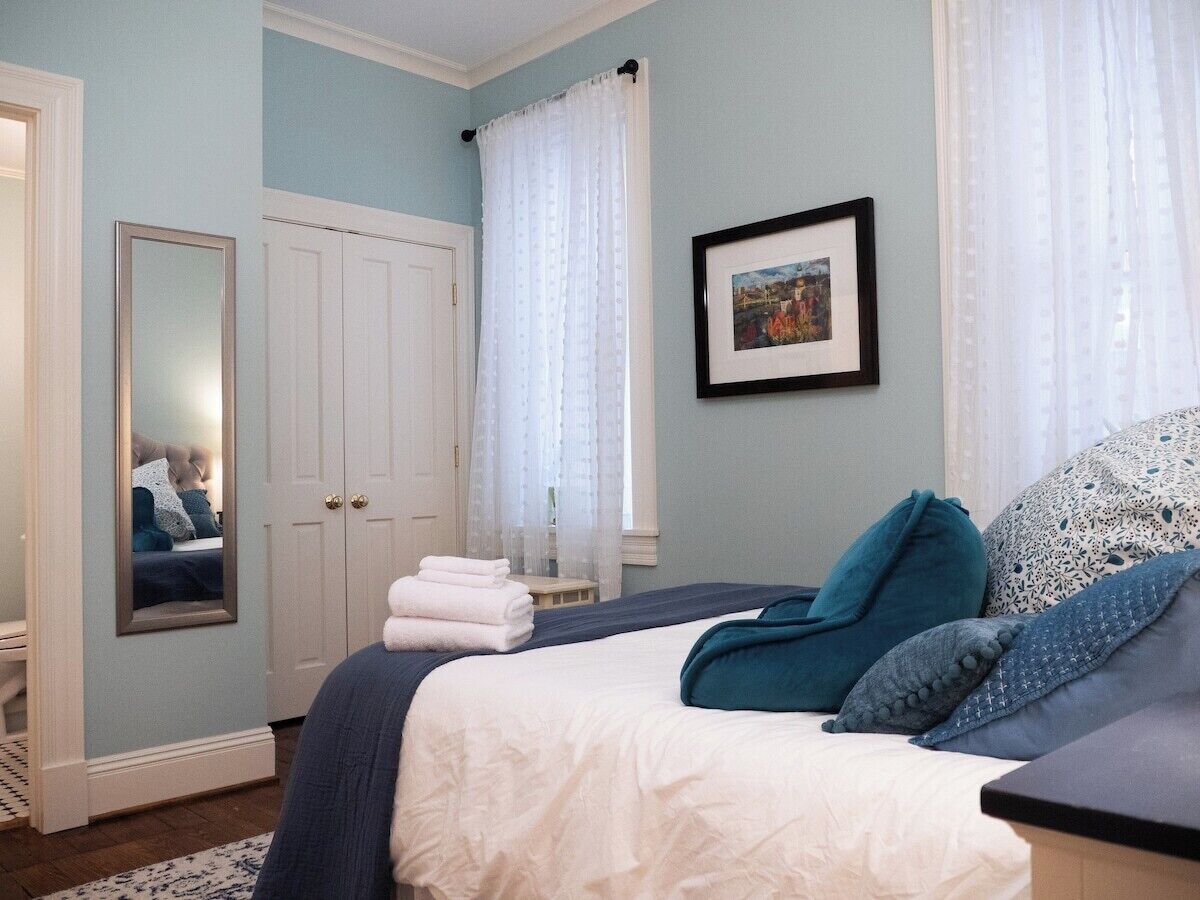 A bedroom with a bed, a mirror, a door, and a framed picture on the wall.