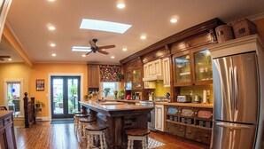 A spacious kitchen with a central island, wooden bar stools, a large refrigerator, and a ceiling fan.