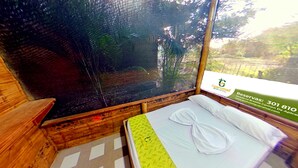Una habitación con una cama, un ventanal con vistas a árboles y suelo de madera.