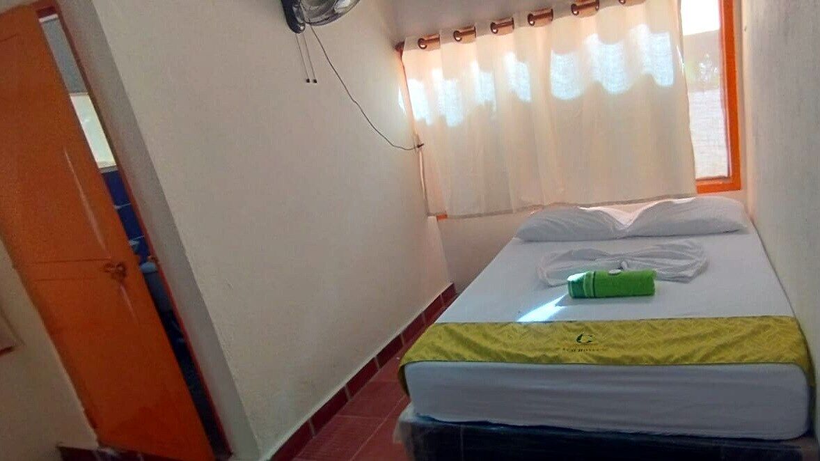 A small room with a bed, a window with curtains, and a wall-mounted fan.