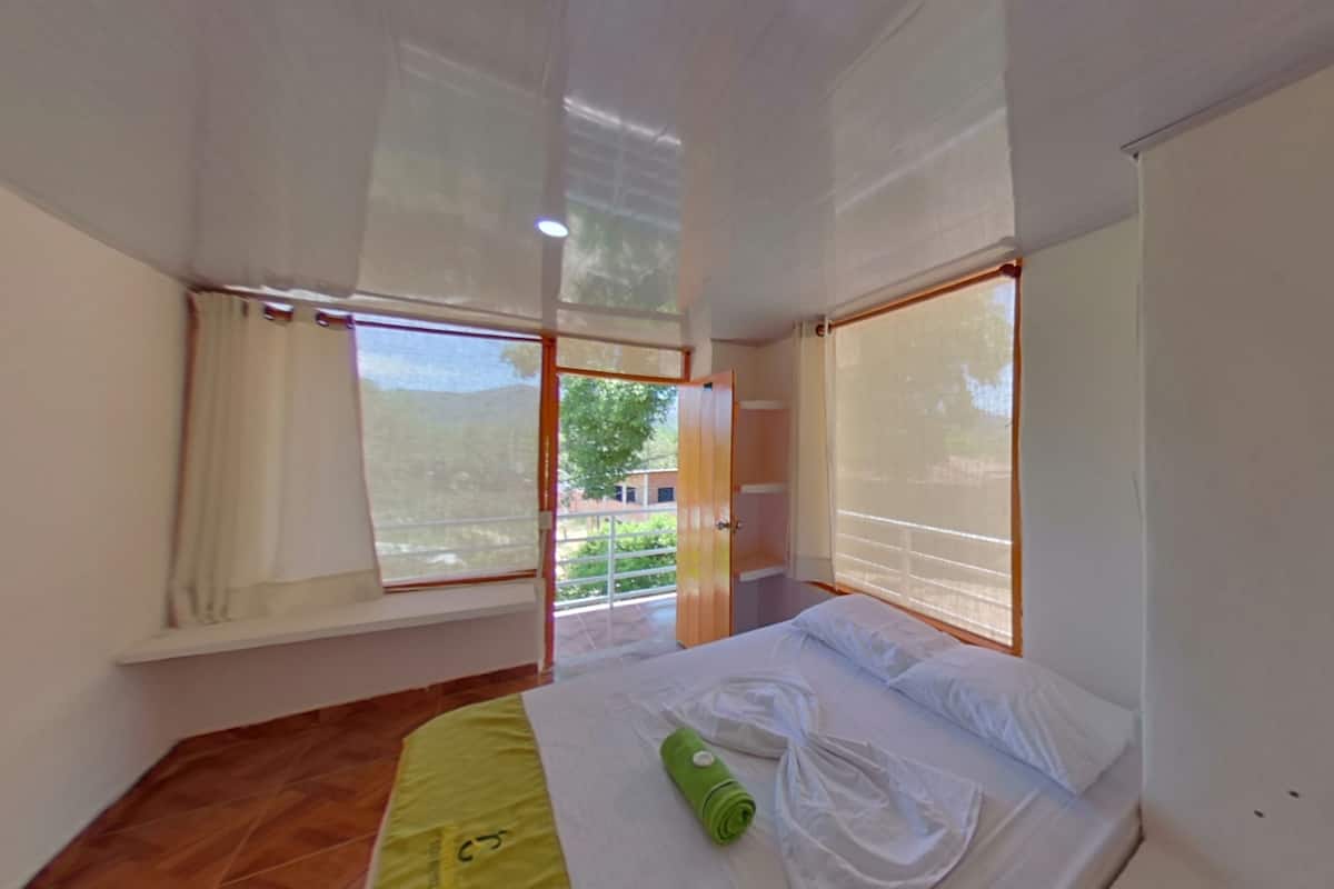 Een slaapkamer met een bed, een raam en uitzicht op groen.