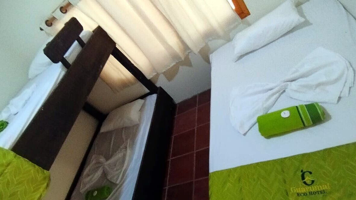 A hotel room with a bed, a green towel, and a green bottle on the bed.