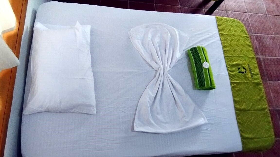 A neatly made bed with white linens and a green towel.