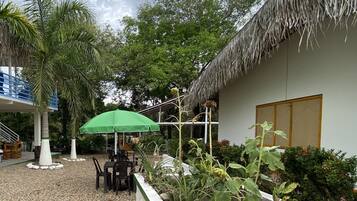 Un patio con un edificio de techo de paja, una sombrilla verde y mobiliario de exterior.