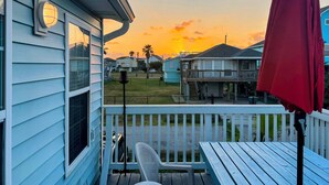 A residential deck with a view of a sunset, a red umbrella, and a white chair. - Enjoy all the history and charm of Galveston Island - a block from the beach! (Galveston)