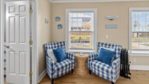 A room with two checkered armchairs, a small woven side table, and a window with blinds. - Enjoy all the history and charm of Galveston Island - a block from the beach! (Galveston)