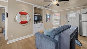 A living room with a grey sofa, a ceiling fan, and a life preserver decoration on the wall. - Enjoy all the history and charm of Galveston Island - a block from the beach! (Galveston)