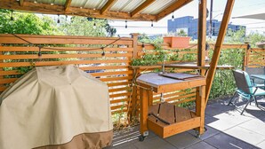 Eine überdachte Terrasse im Freien mit einem Grill, einem Tisch und Stühlen.