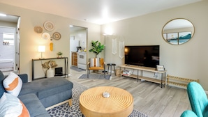Ein modernes Wohnzimmer mit einer Couch, einem Couchtisch, einem Fernseher und einer Küche im Hintergrund.