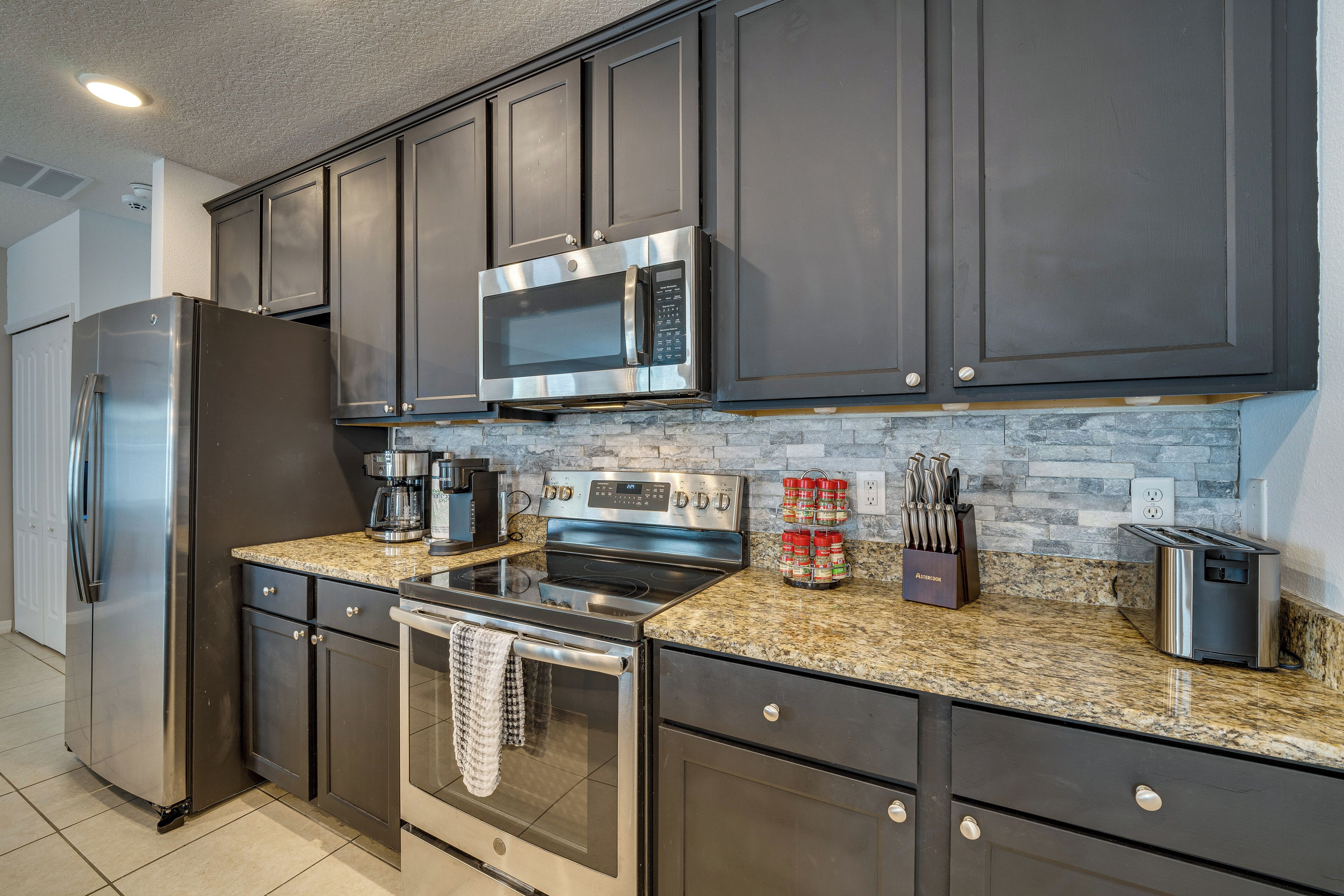 A modern kitchen with dark cabinets, stainless steel appliances, granite countertops, and a stone backsplash.
