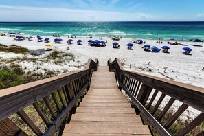 A wooden boardwalk leading to a beach with blue umbrellas and lounge chairs. - Beachside 30A Condo with Private Beach (Santa Rosa Beach)