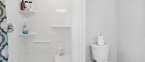 A bathroom with a toilet, a shower, and shelves with toiletries.