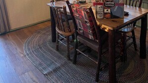 A dining area with a wooden table and chairs, a ceiling fan, and a view of trees through the windows. - Beautiful lakefront cottage, Ambajejus Lake (Northern Piscatiquis Cnt)