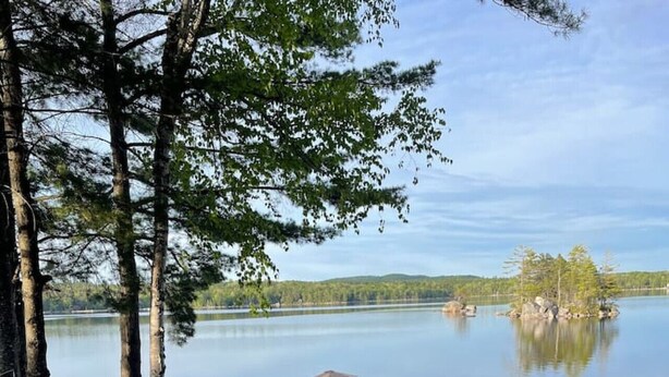 A lakeside picnic area with a red picnic table, black chairs, and a small umbrella. - Beautiful lakefront cottage, Ambajejus Lake (Northern Piscatiquis Cnt)