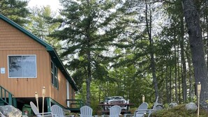 A cabin with a deck area featuring Adirondack chairs and a fire pit. - Beautiful lakefront cottage, Ambajejus Lake (Northern Piscatiquis Cnt)