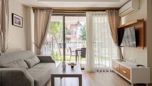 A modern living room with a sofa, a coffee table, and a TV on a wooden cabinet. - Loi Suite (Antalya)