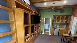 Ein Schlafzimmer mit einem Bett, Holzregalen, einem Fernseher und einer Küchenzeile mit Mikrowelle und Spüle.