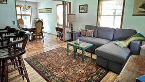 A living room with a sofa, a coffee table, a rug, and a dining area with chairs and a table.