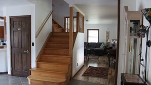 A staircase leading to a second floor, a living room with a sofa and a coffee table, and a kitchen area with cabinets and a door.