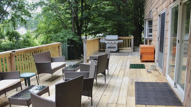 A covered outdoor deck with wicker furniture, a grill, and a sliding glass door leading to a room.