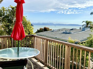 A wooden deck with a glass table and a red umbrella, overlooking a marina with boats and a distant view of the city skyline. - Stay near San Francisco Bay, enjoy our 2+bedroom Tiburon retreat (Tiburon)