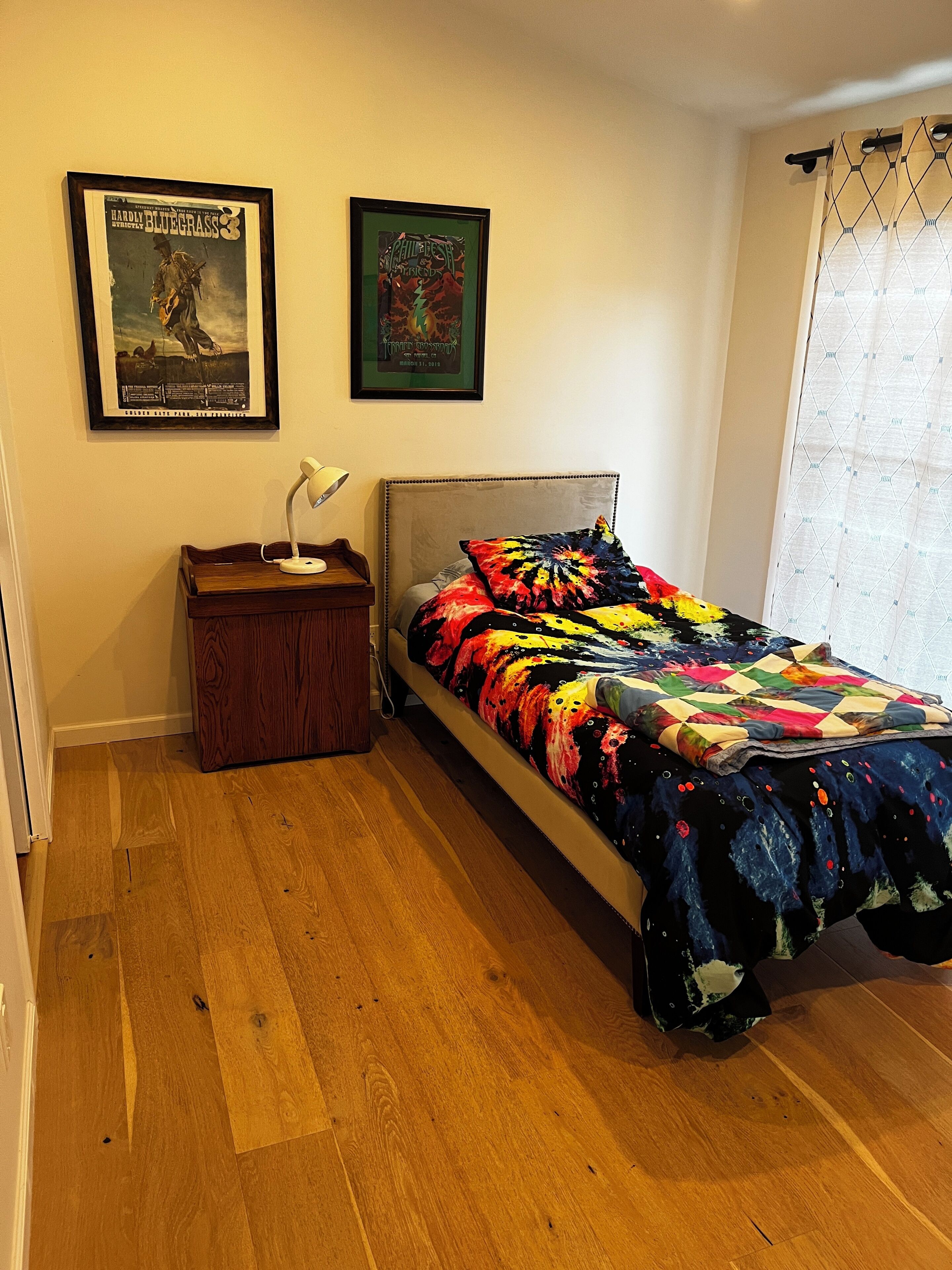 Un dormitorio con una cama, una mesita de noche, una lámpara y dos carteles enmarcados en la pared.