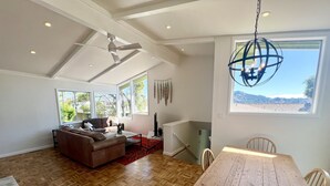 Un salón amplio con suelo de madera, un ventanal grande, un ventilador de techo y un comedor con mesa y sillas de madera.