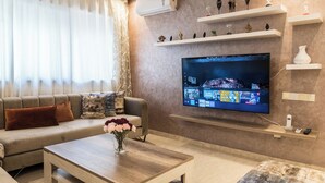 Ein modernes Wohnzimmer mit Flachbildfernseher, einer Couch, einem Couchtisch und dekorativen Regalen.